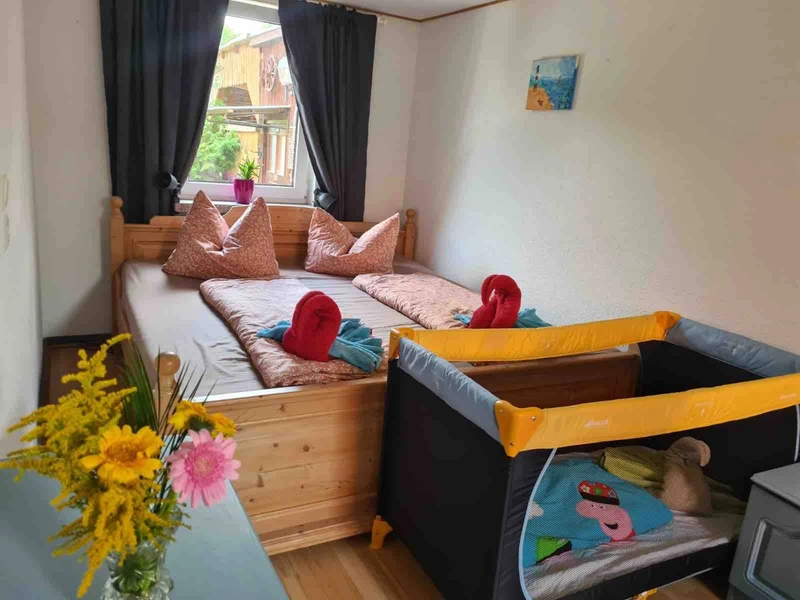 Schlafzimmer mit Doppelbett und aufgestelltem Reisebett für ein Baby